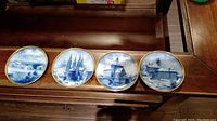 Four blue and white porcelain saucers arranged side by side on wooden surface, details of architectural scenes visible with gold rim.