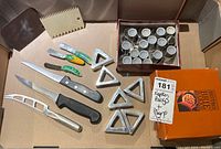 Overview of kitchen knives, napkin ring holders, ceramic cups, note holder, and orange Brie Baker box