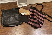 Photo showing an assortment of six purses and totes arranged on floor, including black leather bag with studs, small tan crossbody, black clutch, and black/pink striped Victoria's Secret tote with sequins.