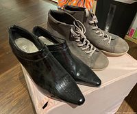 Pair of women's black ankle boots with a pointed toe and side zipper, and men's light brown suede lace-up shoes.