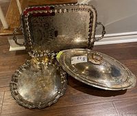 Photo showing three items: large rectangular silver-plated serving tray with handles, oval serving platter with glass insert and hinged lid, and silver-plated gravy boat