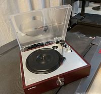 Photo showing full top view of turntable with dust cover open, tone arm positioned on the right, and the black platter visible.