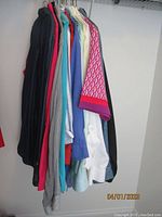 Side view of 14 blouses hanging on hangers, showing various colors including black, red, turquoise, blue, white and patterned fabric