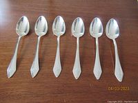 Set of six antique sterling silver teaspoons shown side by side on a wooden surface, each monogrammed "FCK" on the handle tip.