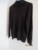 Black Chico's turtleneck long sleeve top displayed on a hanger, showing button details on sleeve cuffs.