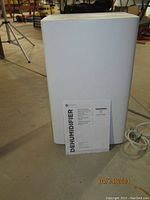 Front view of white GE dehumidifier with owner's manual in front, on concrete floor.