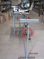Wide view showing the Hitachi compound miter saw mounted on the long Rousseau table with roller and red extension cord beneath.