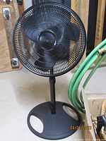 Gray free-standing oscillating fan with protective grill and three blades on plastic pedestal base.