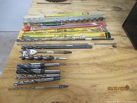 Long wood bits of various types laid on wood table, some loose and some in plastic packaging