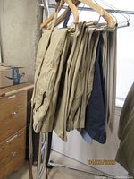 Five pairs of men's casual and work pants hanging on hangers in shades of tan, beige, navy, and light colors.