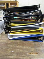 Side view of pile of assorted binders in black, blue, white, and yellow colors, stacked on top of each other on a wooden surface