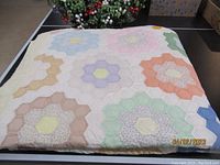 Folded quilt showing pastel hexagonal flower pattern on a dark surface with floral background.