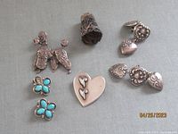 Full lot showing two pairs of earrings, two brooches, and an antique sterling silver thimble arranged on a surface
