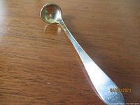 Full view of sterling silver salt spoon showing curved deep bowl and monogrammed handle on wooden surface.