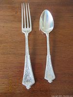 Pair of Tiffany sterling silver fork and spoon displayed side-by-side on wood surface, showing full length and monogrammed handles