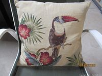 Front view of the jacquard tapestry pillow featuring a toucan sitting on a branch with red flowers and green leaves.