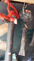 Two gas-powered leaf blowers hanging from hooks, showing full length.