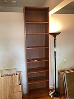 Full view of the tall wooden bookshelf with seven shelves, showing medium brown finish, in a room with a floor lamp nearby.