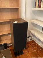 Single upright B&W DM 220 floor standing speaker next to shelving unit, showing height and wood veneer finish with black grille.