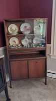 Full view of Mid-Century Modern wood and glass china cabinet with dishes displayed inside the glass shelves.