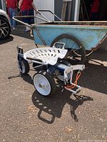 Side view of the Gorilla utility cart with blue metal frame, white metal tractor-style seat, three wheels, and storage basket below seat. Shown outside on pavement with other carts nearby.