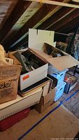 Stacked cardboard boxes and miscellaneous papers in attic space.
