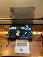 Front view of turntable with hinged dust cover open and instruction manual