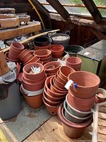 Photo showing stacked terracotta pots and some plastic pots in a shed environment with visible dirt and signs of use.