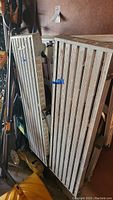 Two aluminum painter's scaffold stands folded and leaning against a wall with visible paint marks and wear