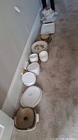 Long view showing multiple stacks of ceramic plates, bowls, and bakeware arranged along a wall on carpeted floor.