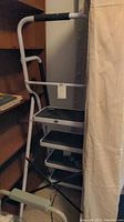Full view of the white foldable stepladder showing four black non-slip steps and padded handles.