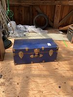 Front view of the vintage blue trunk sitting on wooden floor showing metal latches and lock.