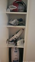 Three handheld vacuum cleaners on shelves in white cabinet.
