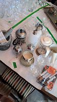 Wide view of the lot on a table, showing granite mortar and pestle, coffee presses, Wedgwood cup, sugar bowls, glass pitcher and other kitchen items.