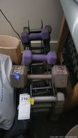 Photo showing purple neoprene dumbbells and metallic hex dumbbells stacked on a black metal rack.