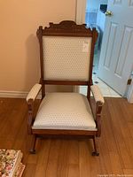Front view showing the carved decorative wooden top rail, upholstered back and seat cushions, padded armrests, and front leg wheels.