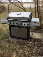 Front view of Brinkmann propane BBQ grill with closed lid showing control knobs, side shelves, cabinet, and overall design.