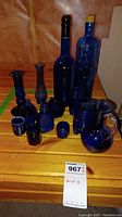 Front view of blue glassware collection showing bottles, decanter, candle holders, mug, and small jar on wooden surface