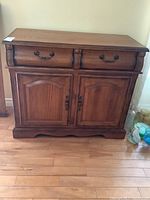 Front view of the solid oak wood cabinet showing two drawers and two doors with metal pull handles on a wood floor.