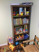 Full view of wooden bookshelf containing children’s books, games, puzzles, assorted toys in bins, and floor toys.