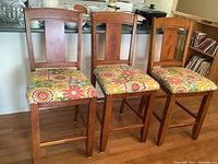 Three solid wood counter height chairs featuring square backrests and colorful floral fabric upholstered seats placed in front of a kitchen counter.