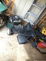 Full side view of green Craftsman mower with black engine and attached black fabric bagger, standing on wooden floor indoors.