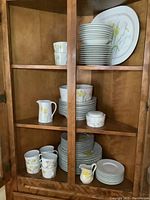 Full view of wooden cabinet with all dinnerware displayed including cups, saucers, plates, bowls, creamer and sugar bowl with daffodil floral design.