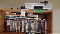 Photo of Toshiba VHS player/recorder on top of bookshelf, with many DVDs and VHS tapes arranged underneath