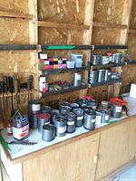 Wide view of metal cans filled with screws, nails, and hardware pieces on shelves and table, with hand files mounted on the wall.