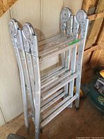 Side view of aluminum multi ladder folded, showing locking hinges and rungs.