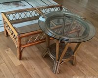 Both rattan tables shown together on wooden floor: one rectangular coffee table and one round side table, each with glass tops.