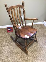 Solid pine wooden rocking chair showing side angle with slatted back, armrests, and curved rockers on beige carpet.