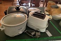 Hamilton Beach white toaster, Beaumark slow cooker, hand grater, Procter Silex popcorn maker and Toastmaster griddle on surface