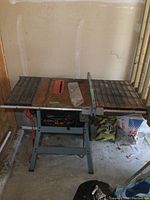Full frontal view of the Delta XL-10 table saw showing the rectangular metal table with rust spots and the saw blade slot, with guide rail attached and metal stand frame.